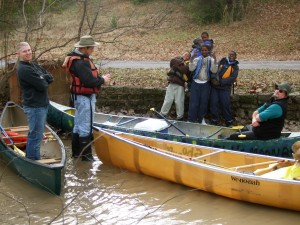 Group of people by a lake with canoes.