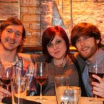 Three friends pose with wine glasses at a restaurant.