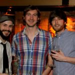 Three men smiling in a bar setting.