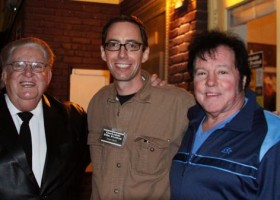 Three men smiling, one with a name tag.