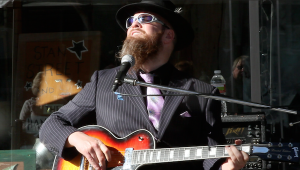 Man with beard plays guitar in a suit.