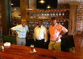 Three men standing at a bar with beer.