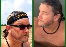 Man in field and lake with beard and necklace.