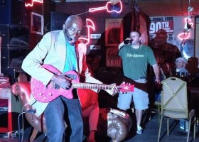 Man plays pink electric guitar in bar