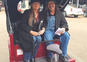 Two people riding in a red motorized rickshaw.