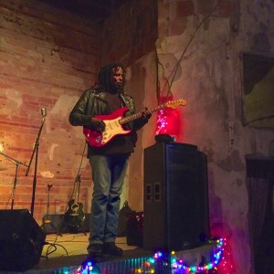 Man playing red electric guitar on stage.