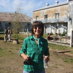 Woman in plaid shirt holding camera and water bottle.