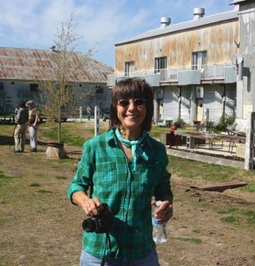 Woman in plaid shirt holding camera and water bottle.