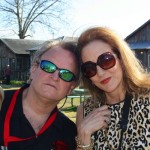 Two people wearing sunglasses smile outside a house.