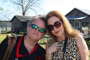 Two people wearing sunglasses smile outside a house.