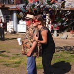 Two people stand near a tree made of bottles.