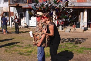 Two people stand near a tree made of bottles.