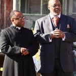 Two men in suits, one in clergy attire.