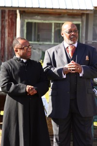 Two men in suits, one in clergy attire.