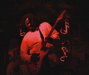 Man plays electric guitar in red light.