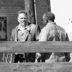 Two men standing by a wooden fence.