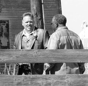 Two men standing by a wooden fence.