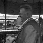 Man in suit laughs under a canopy.