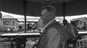 Man in suit laughs under a canopy.