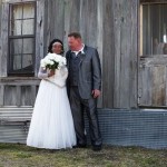 Bride and groom pose in front of wooden building.