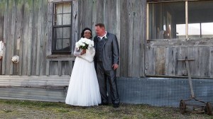 Bride and groom pose in front of wooden building.