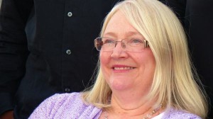 A woman with blonde hair and glasses smiling.