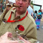 Man with cigar and drinks at a festival.