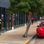 A man in a yellow shirt stands near a red car.