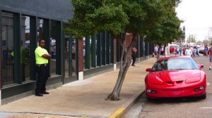 A man in a yellow shirt stands near a red car.