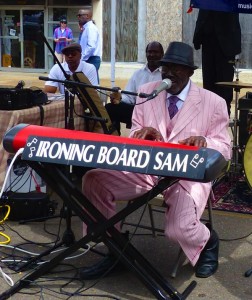 Man in pink suit plays keyboard labeled "Ironing Board Sam"