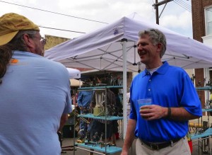 Two men talking under a white canopy tent.