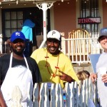 Three men standing by a white fence.