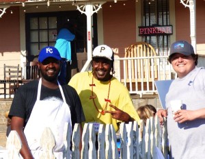 Three men standing by a white fence.