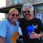 Two men smiling, one holding a cup.