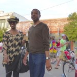 Two people standing on street in front of shops.