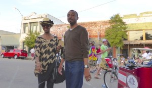 Two people standing on street in front of shops.