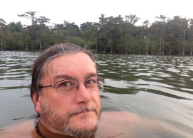 Man with glasses swimming in a lake.