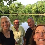 Four friends smiling by a lake.