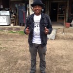 Man in black jacket and hat smiling.