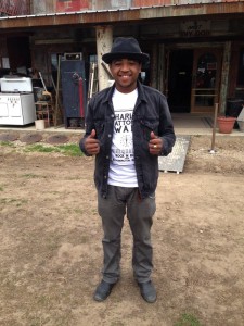 Man in black jacket and hat smiling.