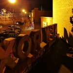 Man standing near a "NEW" sign at night.