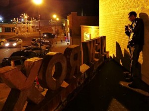 Man standing near a "NEW" sign at night.