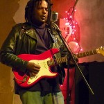 Man playing red electric guitar on stage.