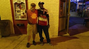 Two men stand smiling outside a building.