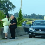 Three people standing by a black Lexus.