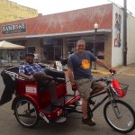 Two men riding a red bike taxi.