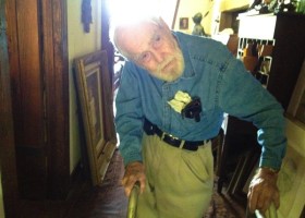 Older man in a blue shirt standing indoors.