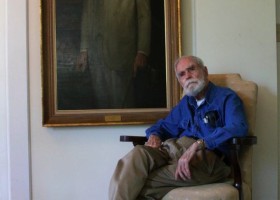 Man in blue shirt sits in chair near portrait.