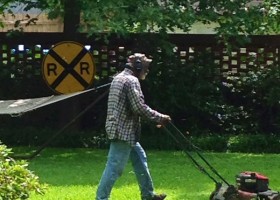 Man mowing lawn with railroad crossing sign.