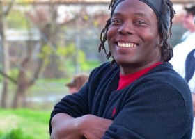 Smiling man with dreadlocks and black sweater.